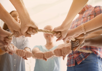 People holding rope together on light background, closeup of hands. Unity concept - obrazy, fototapety, plakaty