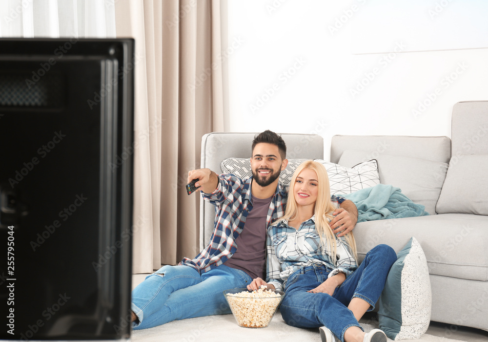 Sticker young couple with bowl of popcorn watching tv on floor at home