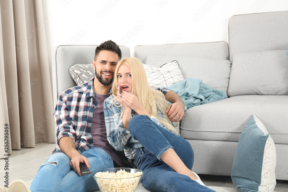 Sticker Young couple with bowl of popcorn watching TV on floor at home