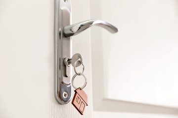 Key with house-shaped trinket in door lock, closeup. Space for text