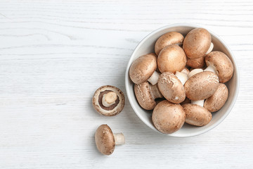 Bowl of fresh champignon mushrooms on wooden background, top view with space for text