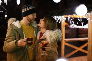 Young couple with cups of mulled wine at winter fair. Space for text