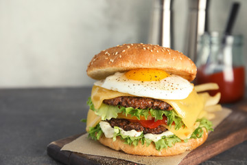Tasty burger with fried egg on wooden board, space for text