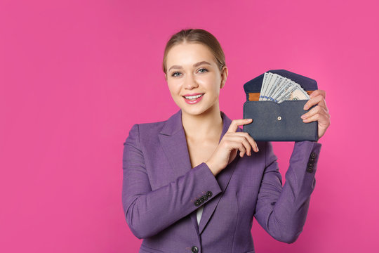 Happy young businesswoman with wallet full of money on color background