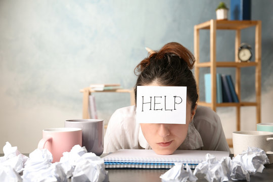 Young Woman With Note HELP On Forehead At Workplace. Space For Text