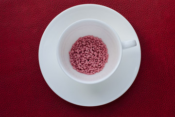 Obraz na płótnie Canvas pink granules in a white cup on a red background