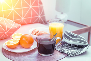 Croissants, black coffee, oranges and juice on the wooden tray. Breakfast in bed, sunny.