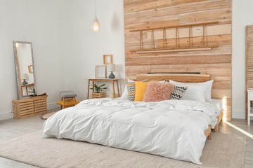 Stylish room interior with comfortable bed near wooden wall