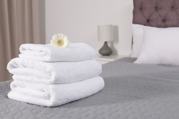 Fototapeta na wymiar Stack of fresh towels with flower on bed in hotel room