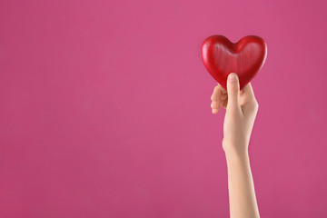 Woman holding decorative heart in hand on color background, space for text