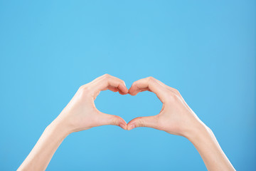 Woman making heart with her hands on color background, closeup