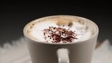 Close up hot coffee cup with milk foam and chocolate decoration rotating on black background