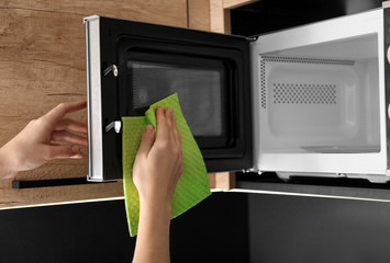 Woman cleaning microwave oven with rag in kitchen, closeup