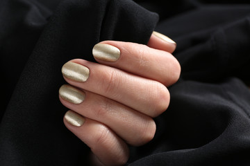 Woman with golden manicure holding black fabric, closeup. Nail polish trends