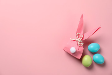 Flat lay composition of Easter bunny gift bag and dyed eggs on color background. Space for text