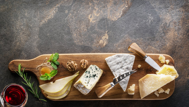 Cheese Platter With Organic Cheeses, Fruits, Nuts And Wine On Stone Background. Top View. Tasty Cheese Starter.