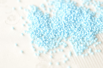 Seed beads light blue color scattered on a textile background close up