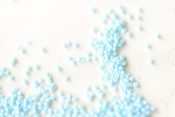 Seed beads light blue color scattered on a textile background close up