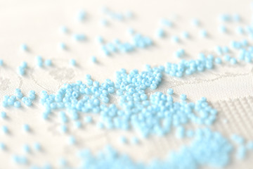 Seed beads light blue color scattered on a textile background close up
