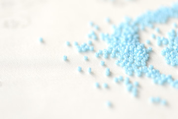 Seed beads light blue color scattered on a textile background close up