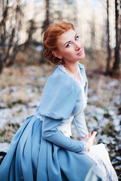 Portrait of a beautiful young girl of European appearance with red hair and blue eyes smiling gently. Bright happy woman in an old national dress sitting in winter park. Illustration to a book