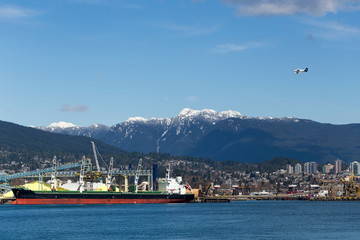 Vancouver seen from the water, with a large ship in the foreground, buildings and mountains in the background and a seaplane in the sky