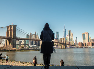 Young Woman by the river in Dumbo looking at Brooklyn Bridge and Cityscape of New York skyline.