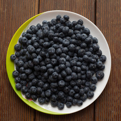 fresh blueberries closeup with dew drops on a plate on a wooden square background