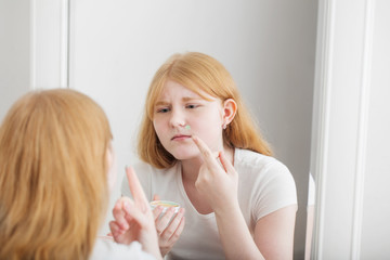 Obraz na płótnie Canvas teen girl examines acne in front of mirror
