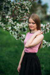 Beautiful blond hair girl standing in front of the blooming tree. Charming lady in dress