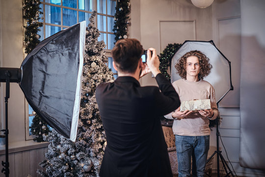 Photoshoot in the studio. Photographer dressed in an elegant costume takes pictures of a curly guy with a gift