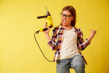 Emancipation woman skillfully holds a drill, standing between the boxes. Studio