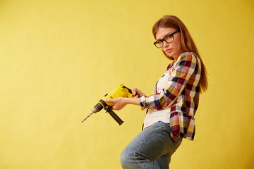 Emancipation woman skillfully holds a drill, standing between the boxes. Studio