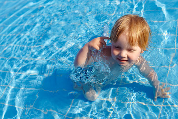 Happy little fair child boy in water in swimming pool