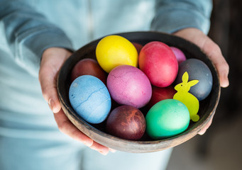 Fototapeta na wymiar Colorful Easter eggs in bowl in woman's hands.