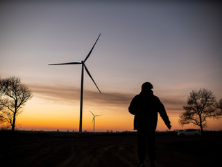 silhouette of a man goes to sunset in the direction of wind turbines