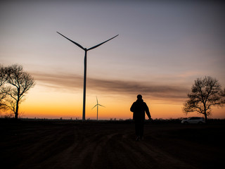 silhouette of a man goes to sunset in the direction of wind turbines