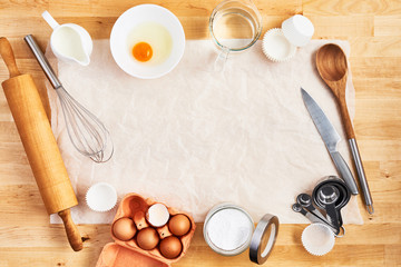 Fototapeta na wymiar Rolling pin, food ingredients and kitchen utensils on crumpled piece of white parchment or baking paper on wooden table. Baking background concept. Top view. Copy space for text and design.