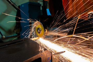 The worker cuts the workpiece with an electric grinder, many sparks fly sideways.