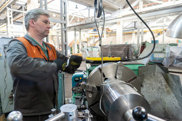 Turner worker manages the metalworking process of mechanical cutting on a lathe.