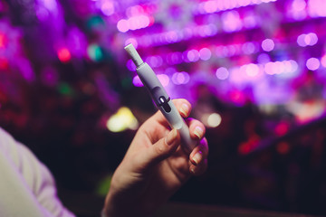 Electronic cigarettes, technology cigarette. Tobacco system IQOS. female hand on blurred background of restaurant