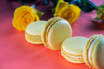 Lemon yellow macaroons on a background of yellow roses on the table in the color of live corals. Delicious French dessert. Close-up.
