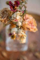 Art photography. Roses withered in a glass vase. Faded roses and dry grass on a wooden surface. Nature wallpaper blurry background. Toned image. Closeup. Soft focus.