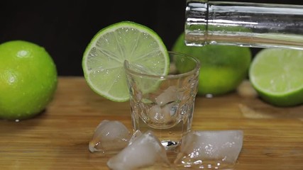 Pour vodka or tequila from a bottle into shot glasses with ice cubes