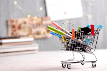 Creative image with stationery in shopping cart and notebooks, gift cards and fairy lights...