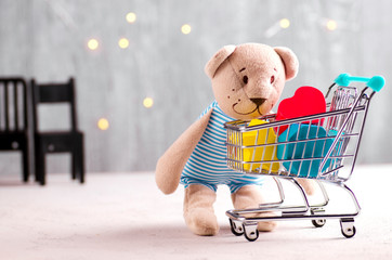Teddy bear looking at shopping cart with children's wooden toys. Fairy lights background