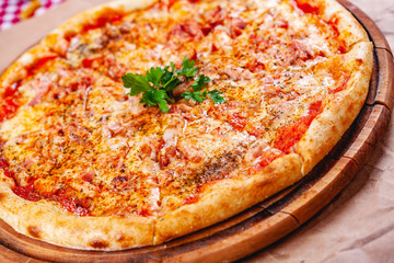 Italian Pizza with bacon, tomatoes and mozzarella cheese on wooden cutting board. Close up