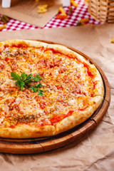 Italian Pizza with bacon, tomatoes and mozzarella cheese on wooden cutting board. Close up