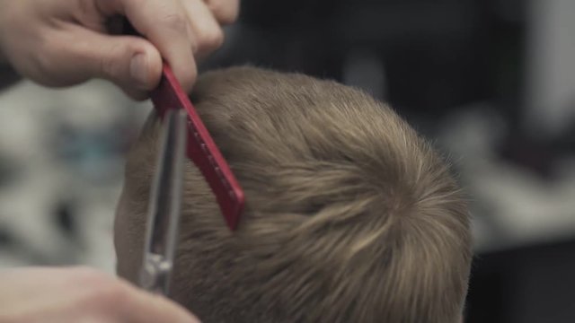 Close up barber cuts hair of client with scissors in slow motion. Barber cuts hair in barbershop. Men's hairstyling and haircutting in barber shop or hair salon