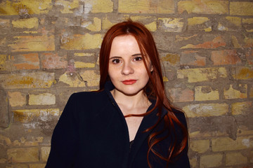 Portrait of a young red-haired girl against an old brick wall.